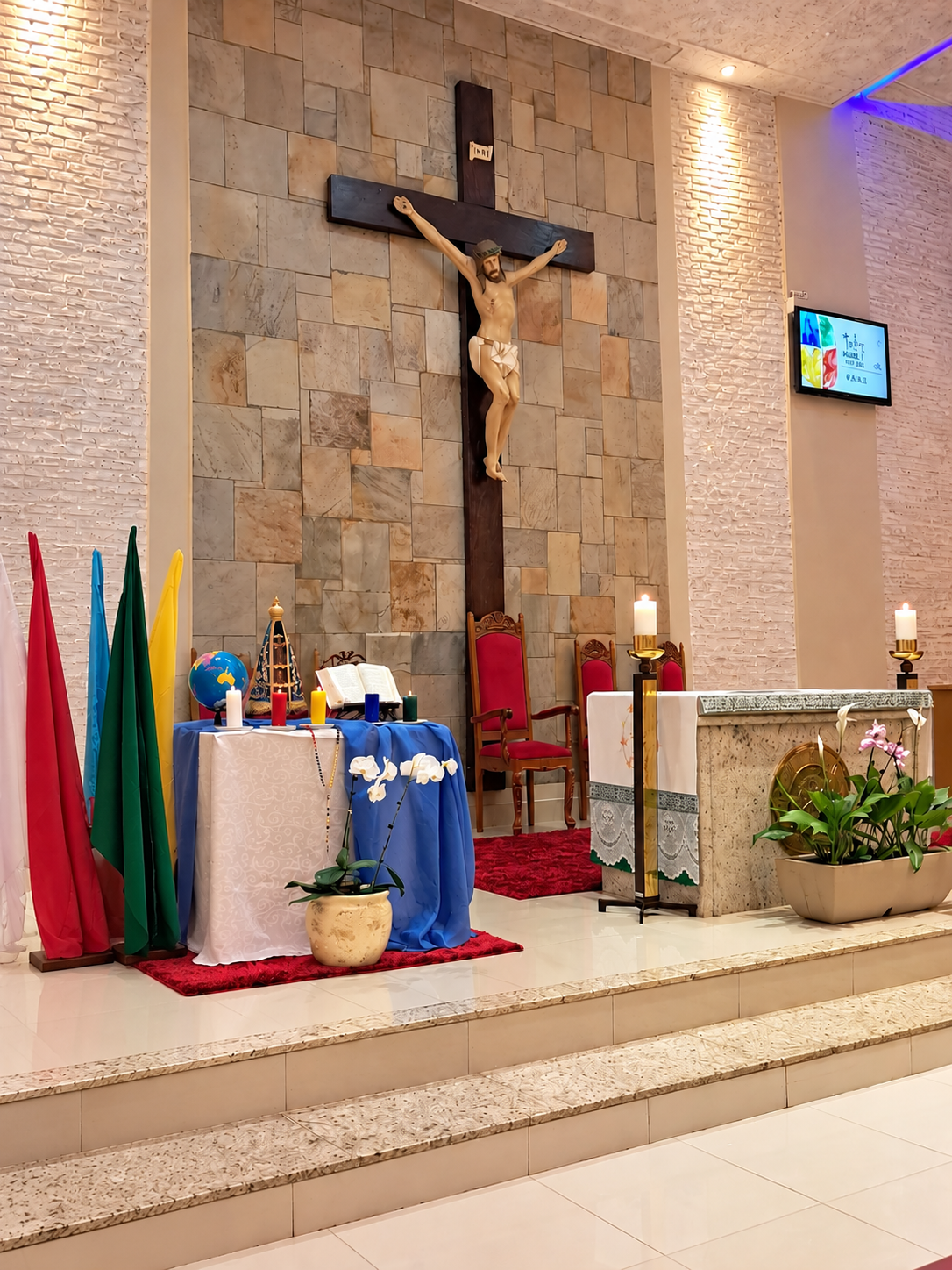 Fotografia oficial do altar da Paróquia Santo André, em Dourados/MS: crucifixo, altar com velas acesas, imagem de Nossa Senhora Aparecida, Bíblia aberta e velas missionárias.