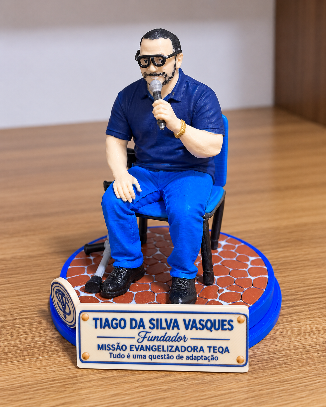Boneco 3D da Missão Evangelizadora TEQA: representação simbólica de Tiago da Silva Vasques, Fundador, sentado em uma cadeira azul com microfone na mão e muleta apoiada ao lado